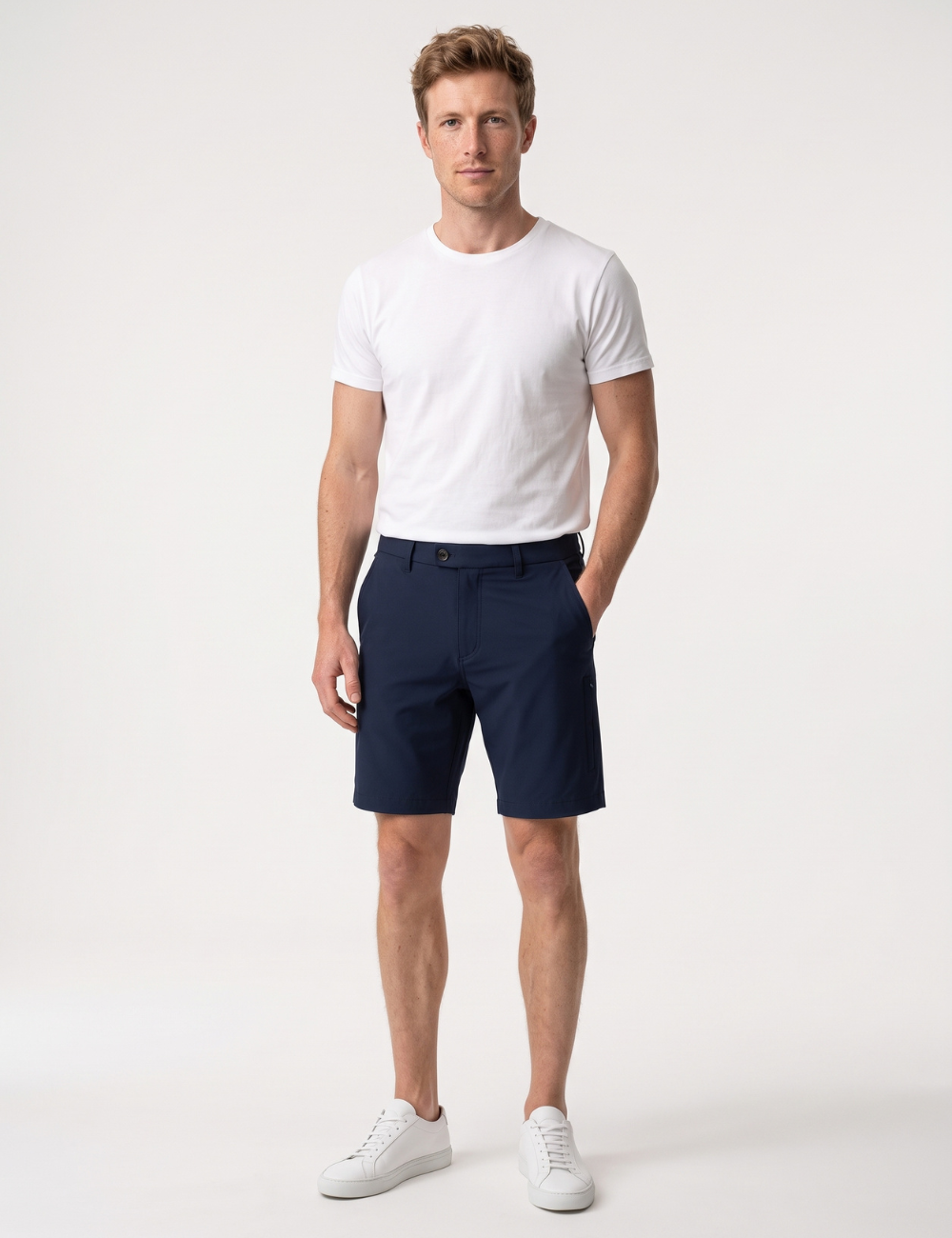 A man modeling a white crewneck t-shirt and navy blue chino shorts, paired with white sneakers, against a plain white studio background. #Color_Navy Blue